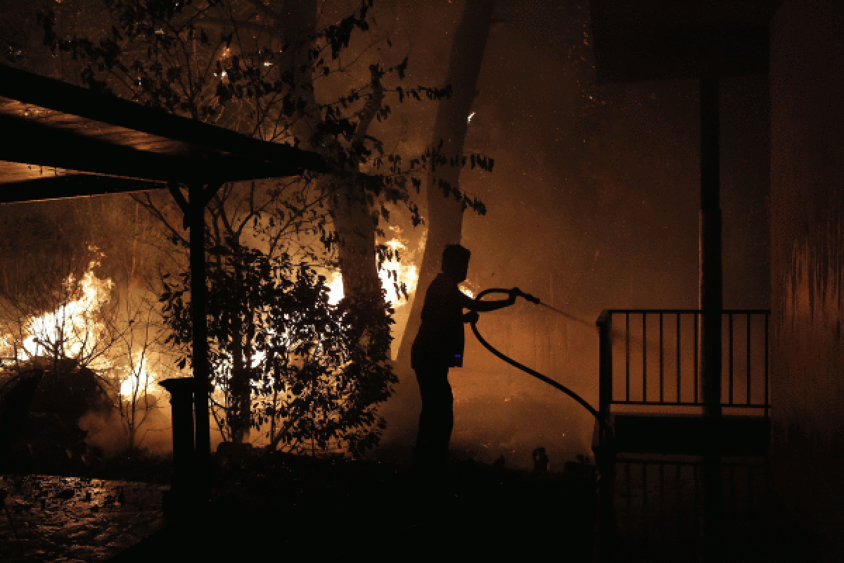 Emakume bat sua itzaltzen saiatzen, etxe atarian, Atenas inguruan, atzo. KOSTAS TSIRONIS / EFE