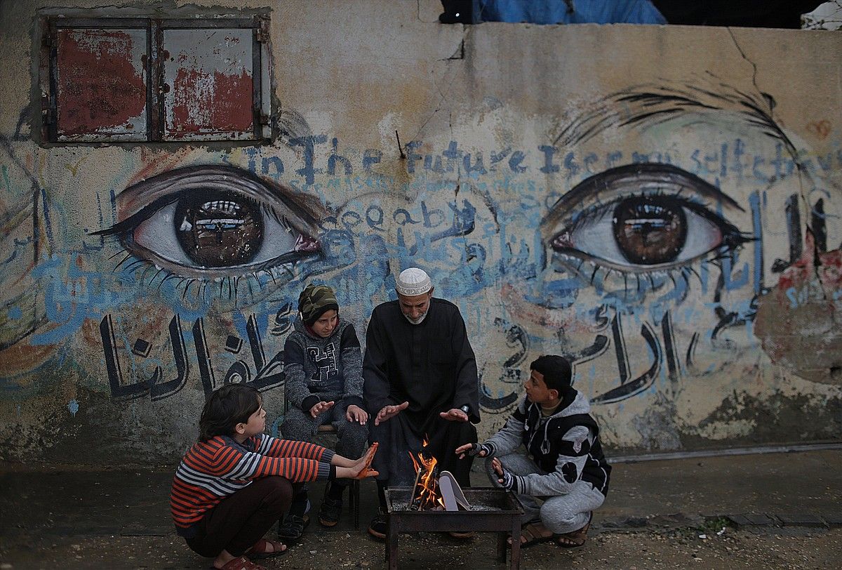 Familia palestinar bat joan den urtarrilean, eskuak berotzen, Beit Hanunen, Gazan. MOHAMMED SABER / EFE.