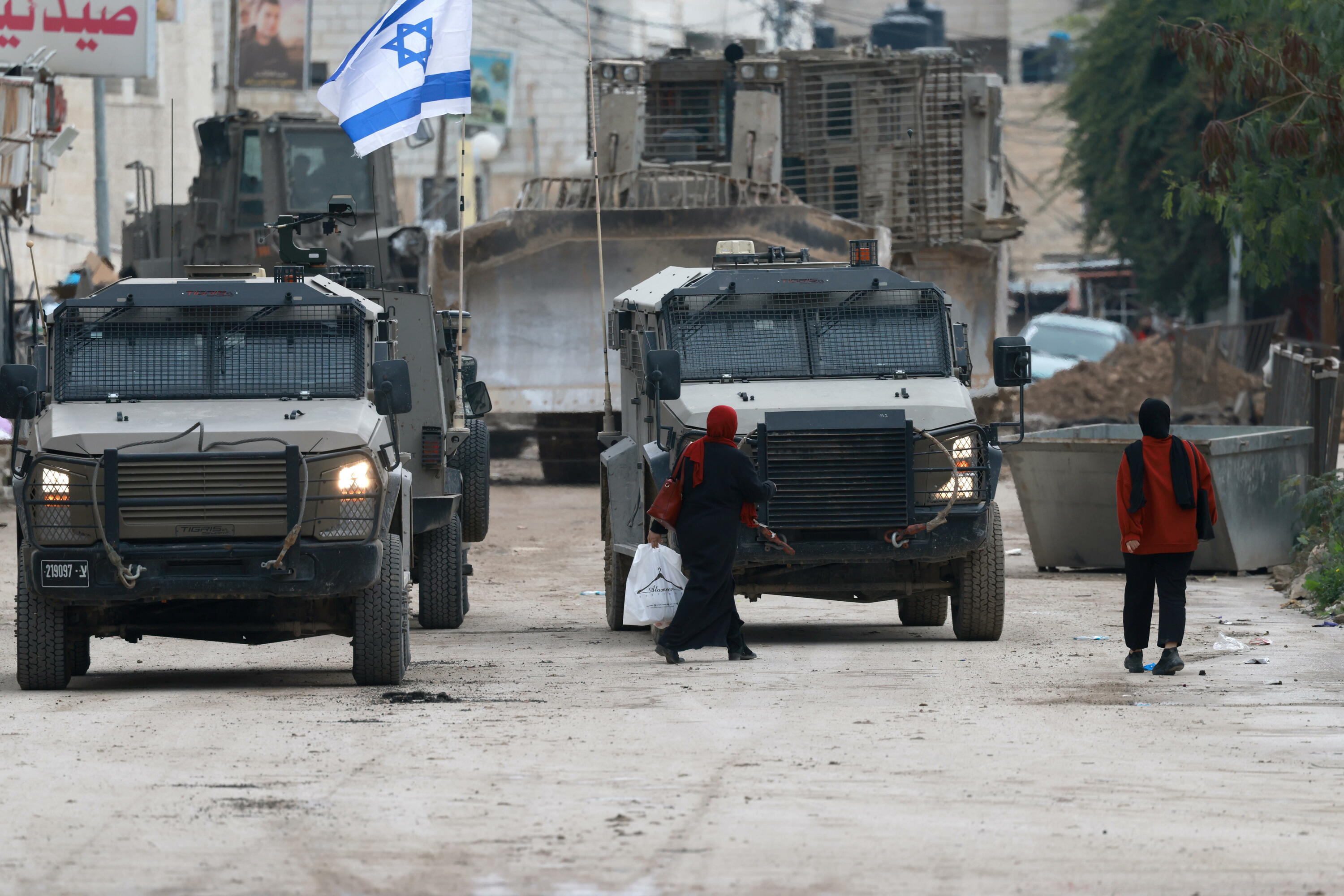 Bi emakume palestinar oinez, Israelgo armadaren ibilgailuen ondoan, gaur, Jeninen. ALAA BADARNEH / EFE